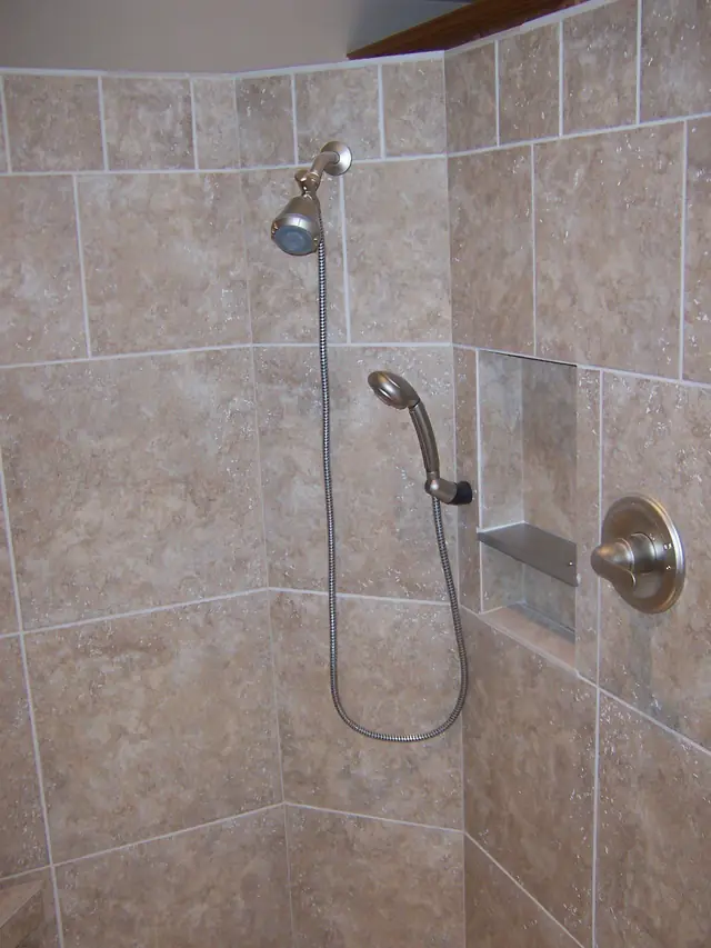 Chrome fixed and handheld shower head pair in a tiled corner shower