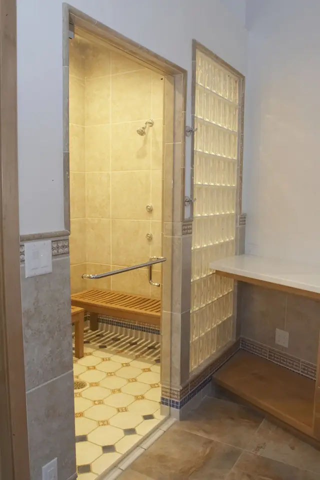 Walk in steam shower and spa room with a glass block wall, teak bench and body sprays
