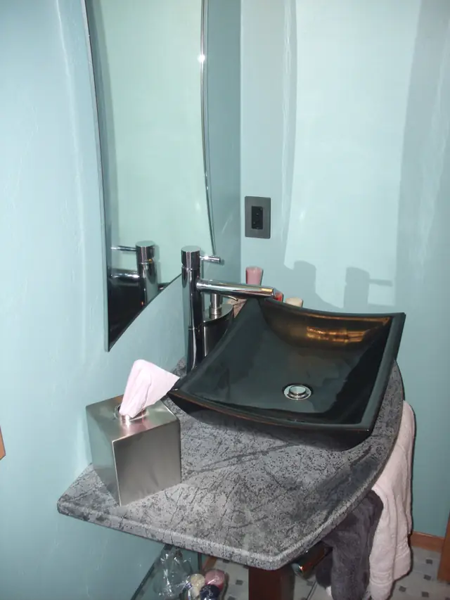 Floating black glass vessel sink on a granite ledge in a modern powder room