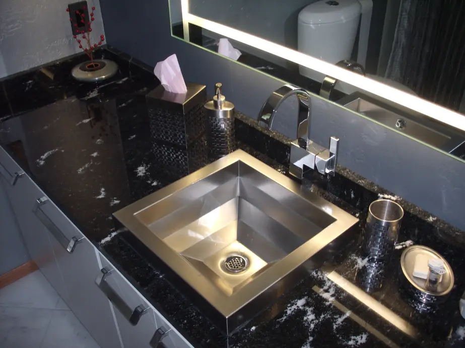 Black granite vanity with a stainless vessel sink, waterfall faucet and backlit mirror