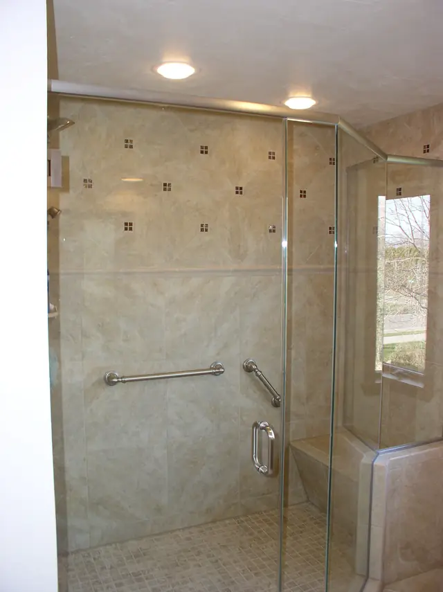 Custom tiled walk in shower with a glass enclosure, grab bars, bench and window